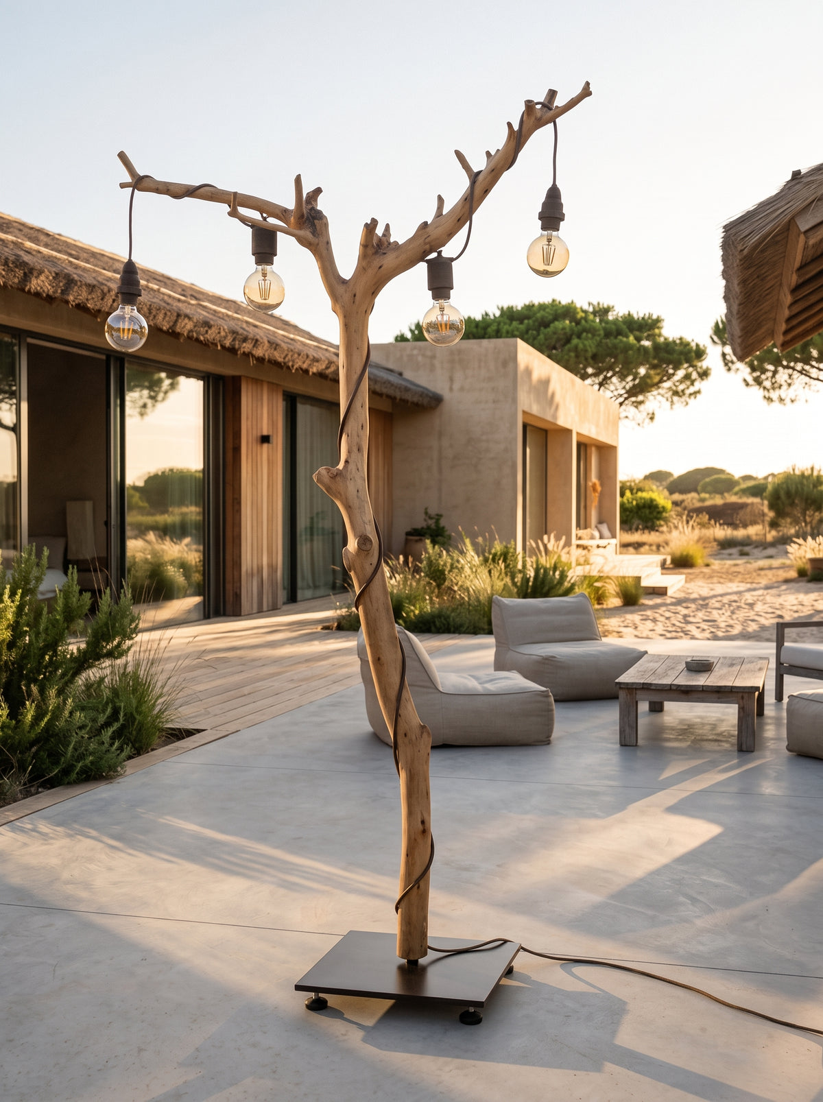 Candeeiro de pé ALCE em tronco de oliveira à luz do pôr do sol, num pátio com sofás de exterior e uma casa ao fundo | LAMS Woodcrafts