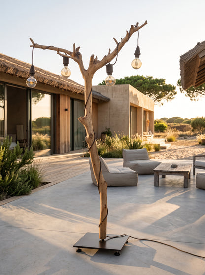 Candeeiro de pé ALCE em tronco de oliveira à luz do pôr do sol, num pátio com sofás de exterior e uma casa ao fundo | LAMS Woodcrafts