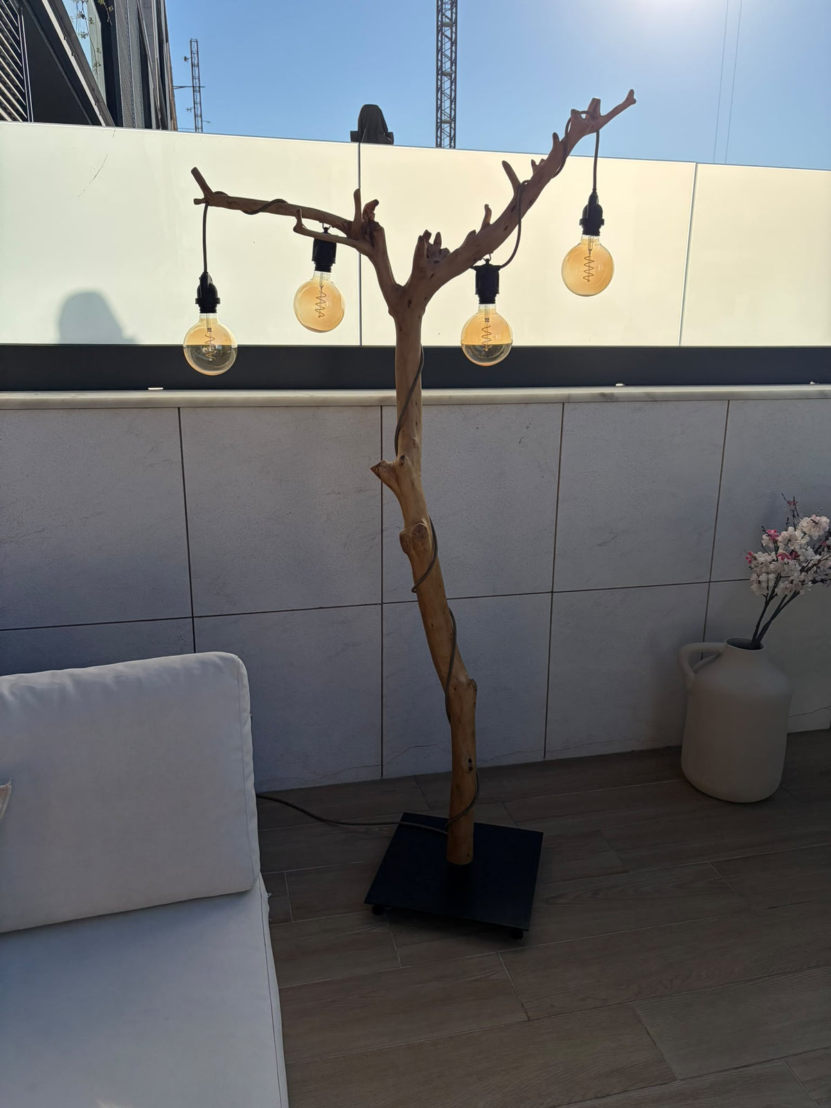 Candeeiro de pé ALCE em oliveira com quatro lâmpadas apagadas, numa varanda ao sol junto a um sofá branco | LAMS Woodcrafts